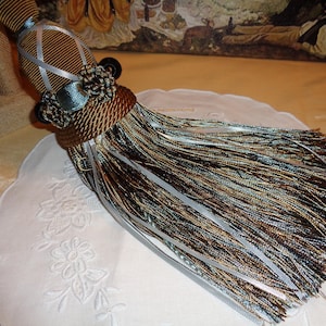 May include: A brown and blue tassel with a white and brown striped ribbon. The tassel is made of multiple strands of brown, blue, and white yarn.