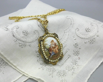 Peut inclure: Un collier vintage doré avec un pendentif ovale représentant une scène peinte de personnes. Le pendentif est encadré de fausses perles et d'une bordure dorée ornée. Le collier repose sur un tissu blanc brodé.