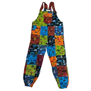 May include: Colorful patchwork overalls featuring a mushroom pattern. The overalls have adjustable straps and a relaxed fit. The design incorporates squares of various colors, including blue, green, orange, and brown, each with a different mushroom illustration.
