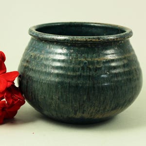 Könnte beinhalten: Eine handgefertigte, teal-farbene Keramikschale mit strukturierter Oberfläche. Die runde Schale hat eine breite Öffnung und wird von einem Cluster leuchtend roter Blumen begleitet, was einen auffälligen Kontrast erzeugt. Ca. 15 cm Durchmesser.