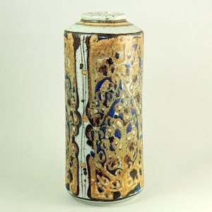 May include: A cylindrical ceramic vase with a textured surface. The vase features a pattern of gold, brown, and blue swirls and dots. The top rim has a gold band. The vase is approximately 12 inches tall.