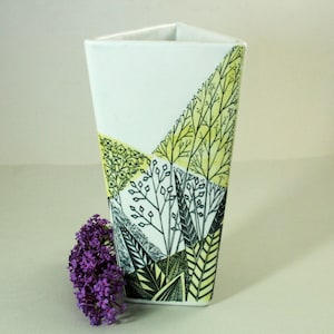 Könnte beinhalten: Eine weiße Keramikvase mit dreieckiger Form und einem geometrischen Muster aus schwarzen und gelben stilisierten Pflanzen.