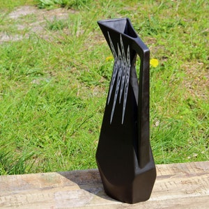 May include: A black ceramic pitcher with a geometric design. The pitcher has a wide base and a narrow spout. The design features white lines that create a pattern of triangles and squares.