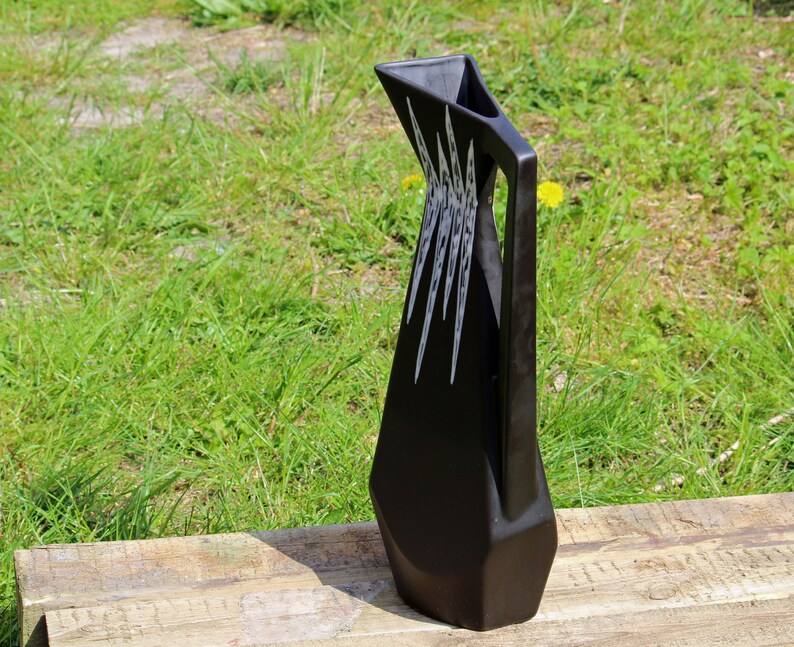 May include: A black ceramic pitcher with a geometric design. The pitcher has a wide base and a narrow spout. The design features white lines that create a pattern of triangles and squares.