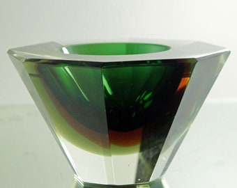 Puede incluir: Un cenicero de vidrio verde con un diseño facetado. El cenicero tiene un interior verde oscuro y una base de vidrio transparente.