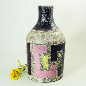May include: A ceramic vase with a geometric design in black, pink, yellow, and white. The vase has a textured surface and a rounded shape.