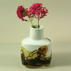 Può includere: Un vaso in ceramica bianca con un design astratto marrone e arancione, che contiene un mazzo di fiori rosa.