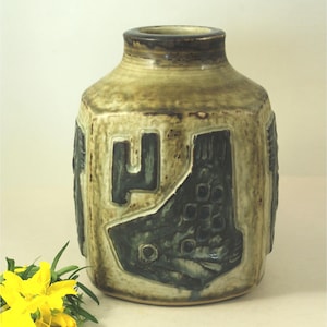Könnte beinhalten: Eine Keramikvase mit einem strukturierten, erdigen Design. Die Vase hat einen abgerundeten Körper mit schmalem Hals und ist mit dunkelgrünen geometrischen Mustern verziert. Die Farbpalette umfasst Braun-, Grün- und Beigetöne.
