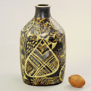 May include: A dark gray ceramic vase with a yellow geometric design. The vase has a rounded body and a narrow neck.
