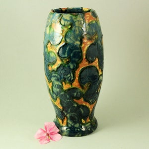 May include: A ceramic vase with a green and orange abstract pattern. The vase is oval shaped and has a wide mouth.