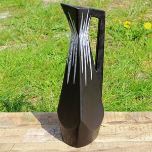 May include: A black ceramic pitcher with a geometric design and white accents. The pitcher has a handle and a spout.