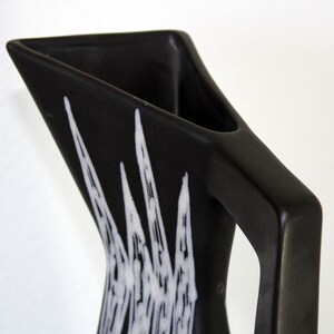 May include: Black ceramic pitcher with a white geometric design. The pitcher has a triangular shape and a handle.