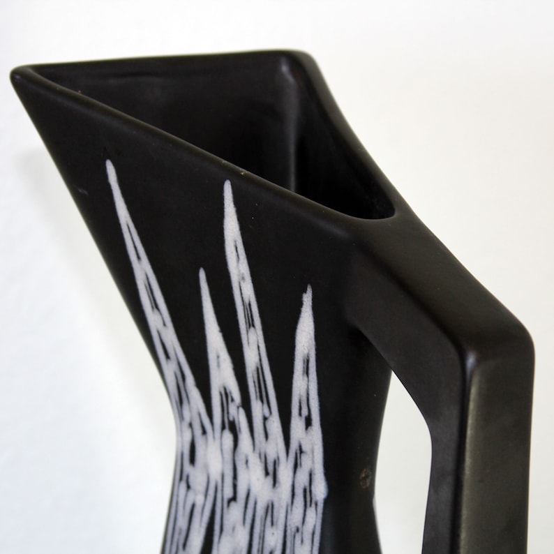 May include: Black ceramic pitcher with a white geometric design. The pitcher has a triangular shape and a handle.