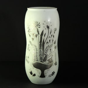 May include: Cream-coloured vase with a black rim and a decorative floral design. The vase features a stylized illustration of various plants and flowers in silver and black, including ferns and seed heads.