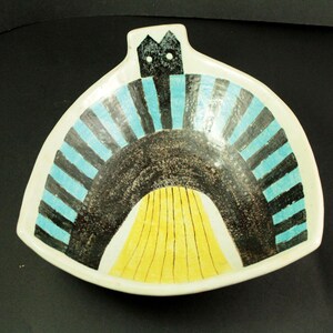 May include: A ceramic serving dish with a unique design. The dish features a white base with a black, blue, and yellow pattern. The design includes a black arch with blue and black stripes, and a yellow section at the bottom. The dish has a handle.