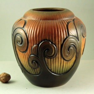 May include: A brown ceramic vase with a textured surface and a swirling design. The vase has a dark brown base and a lighter brown top.