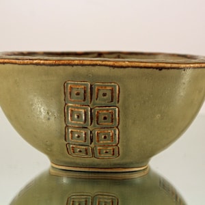 May include: A green ceramic bowl with a brown rim and geometric design. The bowl is glazed and has a matte finish.