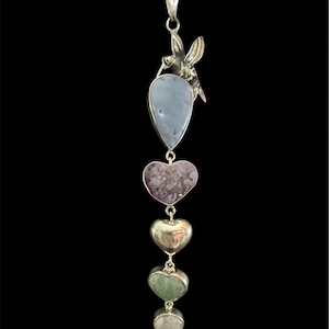 Puede incluir: Un collar con colgante de plata con un motivo de colibrí y una serie de amuletos de piedras preciosas. Los amuletos incluyen una piedra azul en forma de lágrima, una amatista en forma de corazón, tres corazones de plata y piedras verdes, grises y rojas en forma de corazón.