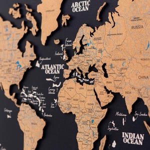 May include: A framed world map with a dark blue backdrop and a detailed, three-dimensional map made of a light brown material. The map includes labels for oceans and countries, with a compass rose in the lower left corner.