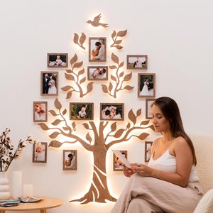 Puede incluir: Una decoraci&oacute;n de pared de &aacute;rbol geneal&oacute;gico de madera con luces y varias fotos enmarcadas de una familia. Una persona est&aacute; sentada en una silla blanca y mirando una foto.