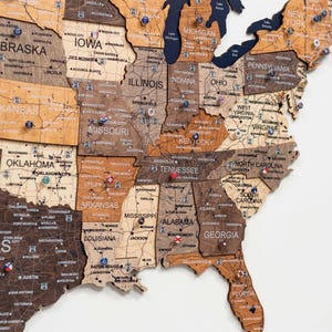 May include: A wooden map of the United States with state outlines and city names. The map is made of various shades of brown wood, with pins marking locations. The map is a decorative piece for travel enthusiasts.