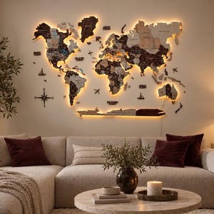 May include: A large, multi-layered wooden world map wall art piece featuring varying shades of brown wood, illuminated by warm LED backlighting. The map includes cut-out continents, islands, and text labels for oceans and regions, mounted on a wall.