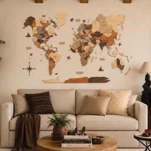 May include: A large, multi-piece wooden world map wall art installation featuring various shades of brown and tan wood tones, mounted on a wall above a beige sofa. The map includes detailed continents, islands, and small decorative wooden icons.