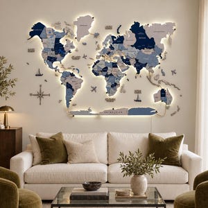 May include: A large, multi-layered wooden world map wall art piece featuring various shades of blue and grey. The map includes integrated LED backlighting, decorative wooden icons of ships and planes, and a compass rose, all mounted on a wall.