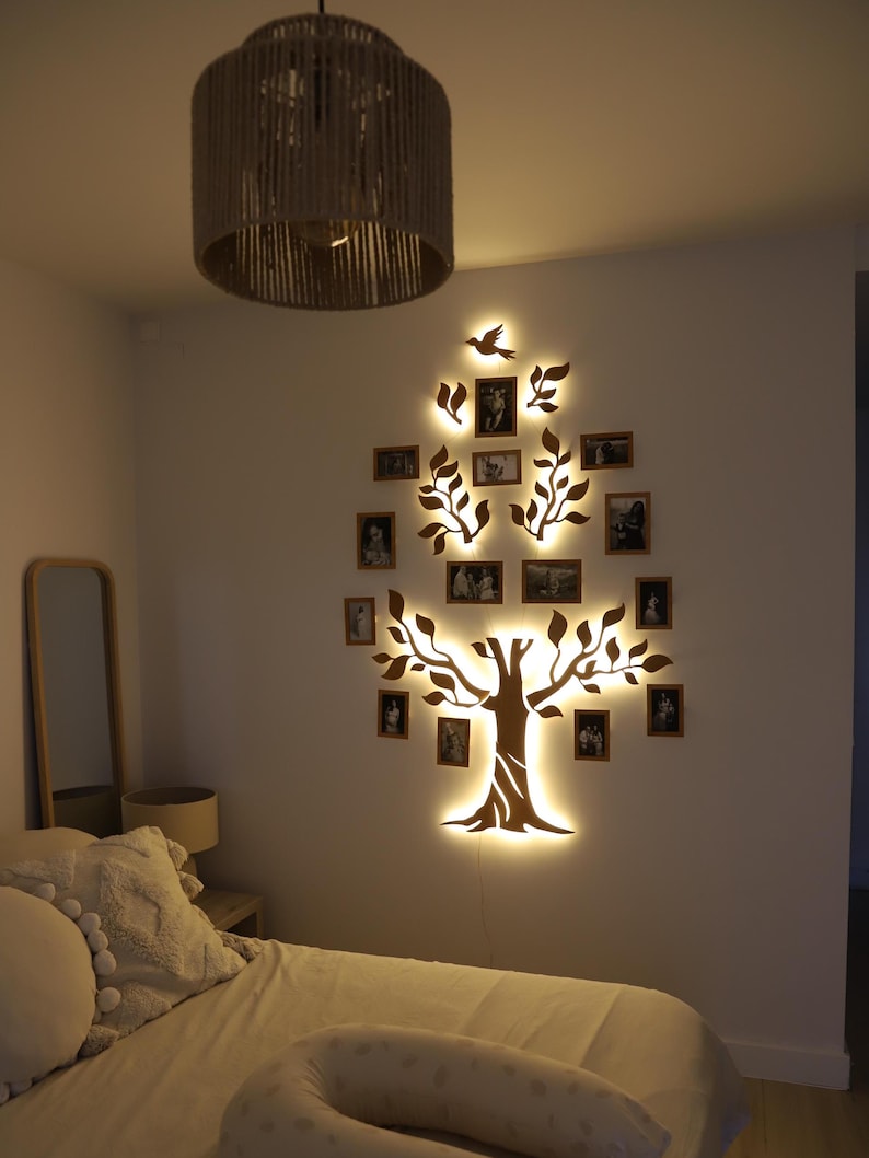 Puede incluir: Una pieza de arte de pared de madera con forma de &aacute;rbol con ramas y hojas. El &aacute;rbol est&aacute; iluminado con luces LED blancas c&aacute;lidas. Hay peque&ntilde;os marcos de fotos colgados de las ramas. El &aacute;rbol est&aacute; montado en una pared blanca en un dormitorio.