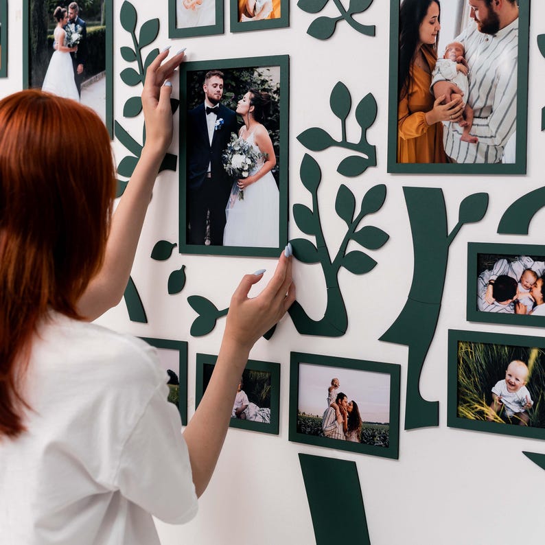 May include: A white wall with a green tree-shaped frame holding various photos. The photos are of a couple, a family, and a baby. The frame is made of wood and has a rustic look.