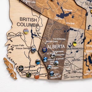 May include: A detailed wooden map of Canada, showing provinces and cities, with pins marking locations. The map displays the text "BRITISH COLUMBIA" and "ALBERTA". The map has various colorful pins indicating places.