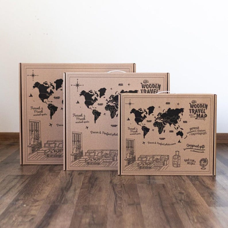 May include: Three rectangular cardboard boxes of varying sizes, each featuring a black printed world map, a compass rose, and illustrations of a living room interior. The text reads Wooden Travel Map, Travel & Mark visited spots, and Decor & Perfect photo zone.