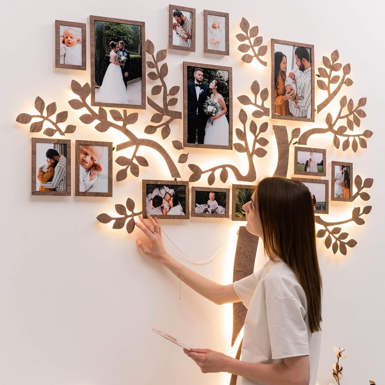 May include: A wooden family tree wall decor with a light brown finish and a white background. The tree is decorated with multiple framed photos of different people, including a couple, a baby, and a family.