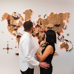 May include: A large, multi-layered wooden world map wall art piece featuring various wood tones, engraved country names, and integrated warm LED backlighting. A decorative compass rose is positioned to the lower left of the map continents.