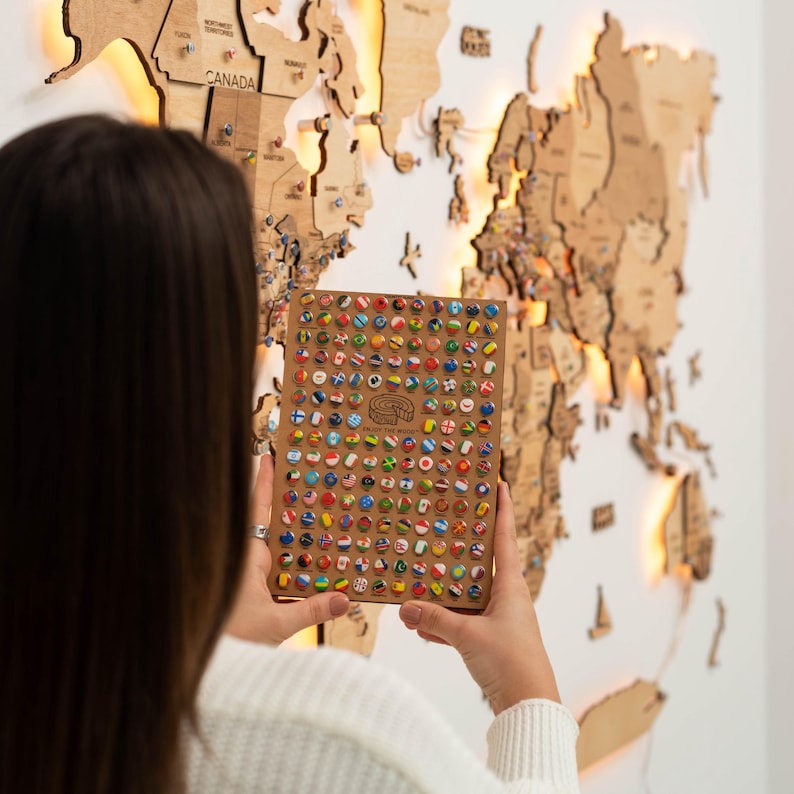 May include: A close-up of a wooden board with a grid of small, colourful flags representing different countries. The flags are arranged in a spiral pattern. The board is being held by a person, but their face is not visible.