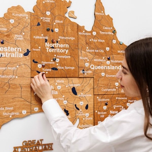 May include: A large wooden wall map of Australia featuring engraved state names, major cities, road networks, and highway markers. The map is composed of multiple wood panels and includes small circular pins placed on various locations.