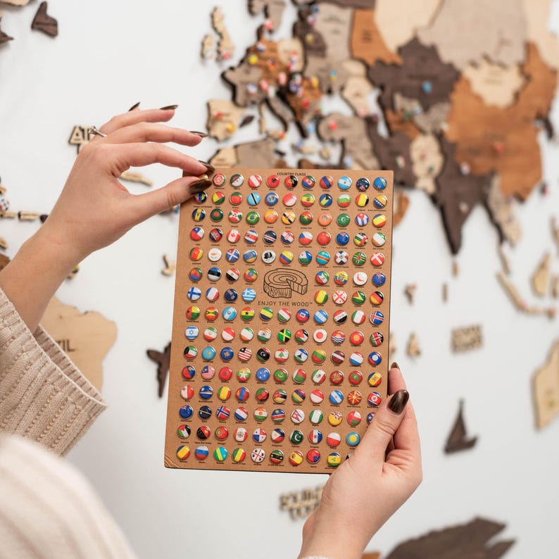 May include: A close-up of a wooden board with a grid of small round pins featuring flags of different countries. The board is labelled "Enjoy the World".