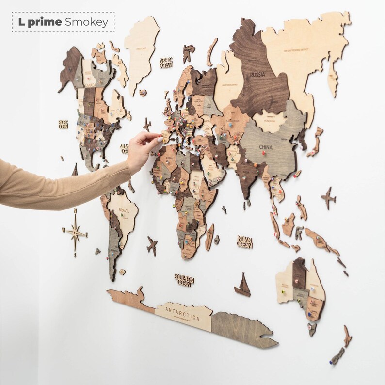 May include: A large wooden world map wall art piece labeled L prime Smokey, featuring laser-cut continents in varying shades of brown and beige wood. The map includes engraved country names, ocean labels, a compass rose, and small decorative wooden airplanes.
