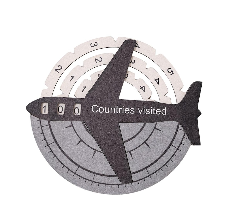 May include: A black airplane-shaped tracker with the text "Countries visited" and three numerical windows displaying "1 0 0". It features rotating white circular dials with numbers and a grey circular base with markings resembling a compass.