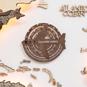 Peut inclure: Décoration murale en bois sur le thème du voyage, avec un design de boussole et le texte "Pays visités". La boussole indique "11" pays visités. Comprend des découpes en bois de pays et le texte "Atlantic Ocean".