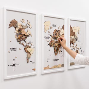 Peut inclure: Trois cartes du monde en bois encadrées de cadres blancs. Les cartes sont faites de différentes nuances de bois et comprennent des épingles marquant les lieux. La première carte montre l'Amérique du Nord et du Sud, la seconde l'Europe et l'Afrique, et la troisième l'Asie et l'Australie.