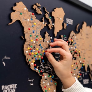 May include: A cork world map with colourful push pins marking locations. The map is mounted on a dark blue background. The map includes the text "PACIFIC OCEAN" and "ARCTIC OCEAN".