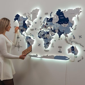 May include: A large, multi-layered wooden world map wall art piece featuring various shades of blue and white. The map includes LED backlighting, labeled continents, oceans, and small decorative icons like airplanes and ships, with Antarctica at the base.