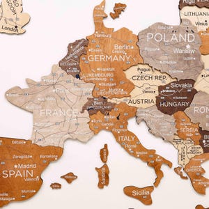 May include: A wooden map of Europe, featuring countries in various shades of brown and tan. Major cities are labeled with text. The map is a decorative piece, suitable for home decor or educational purposes.