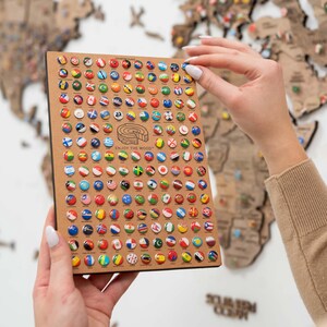 May include: A close-up of a wooden board with a grid of small round pins, each featuring a different country's flag. The board is labelled "COUNTRY FLAGS" and includes the text "ENJOY THE WOOD".