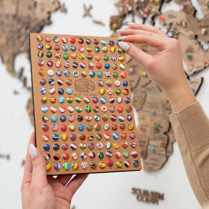 May include: A close-up of a wooden board with a grid of small round pins, each featuring a different country's flag. The board is labelled "COUNTRY FLAGS" and includes the text "ENJOY THE WOOD".