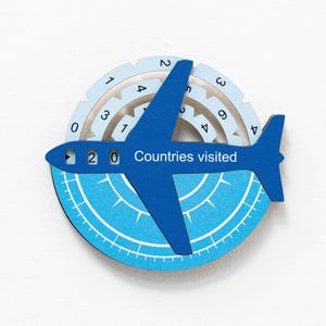 May include: A blue airplane-shaped travel tracker with the text "20 Countries visited." The tracker is set against a light blue and white background with a circular design and numbers around the edge.