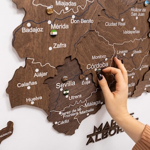 Peut inclure: Une carte en bois brun fonc&eacute; de l'Espagne avec des noms de villes en blanc. Une main place une &eacute;pingle d&eacute;corative sur C&oacute;rdoba. La carte pr&eacute;sente les r&eacute;gions et les villes du pays. Le mot 'MAR ALBOR' est visible.
