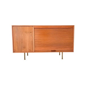 May include: A mid-century modern wooden cabinet with a sliding door and a single door on the left side. The cabinet has brass legs and a brass handle on the single door.