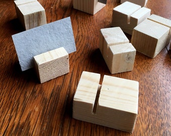 May include: A collection of small, unfinished wooden blocks with a vertical slot cut into the top. Some blocks hold gray rectangular cards. The blocks are scattered on a dark wooden surface, likely a table.
